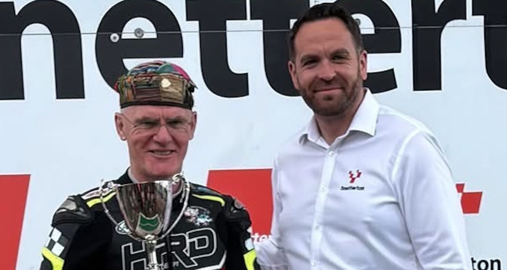 RatMally brand ambassador Mike Edwards holding the 75th Anniversary Snetterton Circuit trophy in the paddock next to his racing gear.